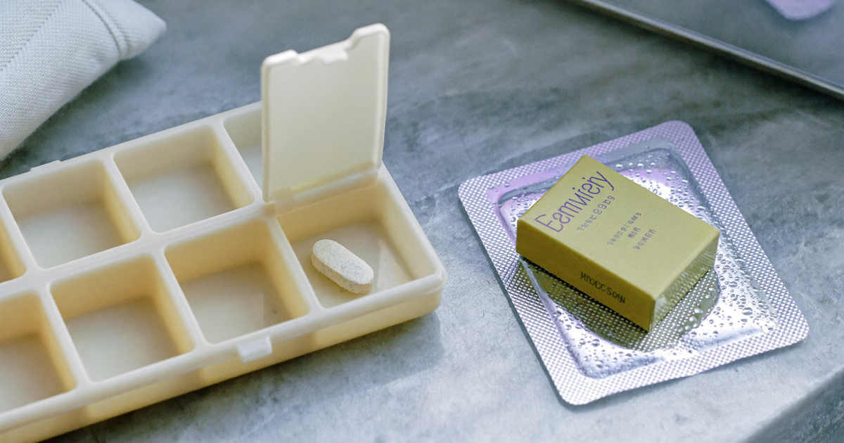 An unbranded extended-release tablet in a weekly pill organiser next to a refrigerated prefilled syringe, comparing oral JAK inhibitor and injected IL-12/23 biologic treatment for Crohn's disease