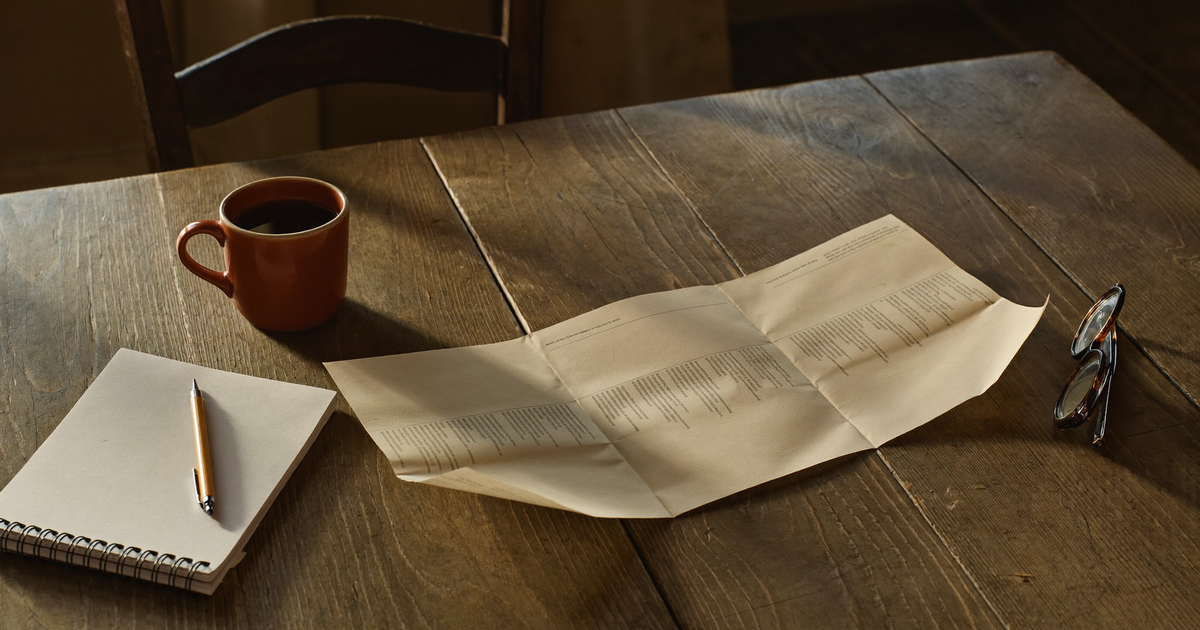 An unbranded prescribing information leaflet open on a kitchen table next to a notebook of questions, representing the Rinvoq vs Stelara boxed warning gap and the safety monitoring each drug requires in Crohn's